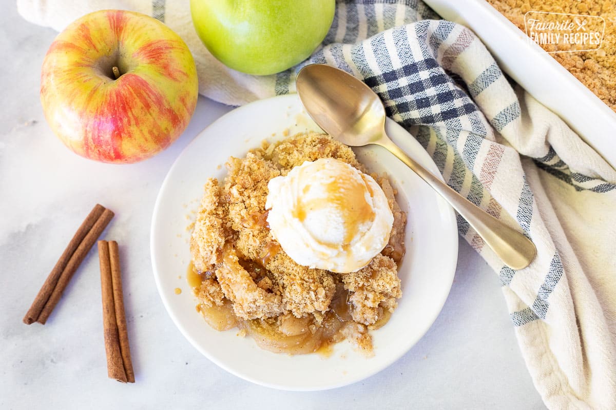 Apple Crisp resting on a plate with vanilla ice cream and caramel sauce. Spoon is also resting on the plate.