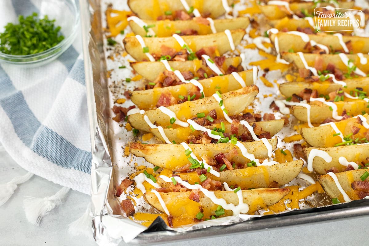 Loaded Potato Wedges on a baking sheet with bacon, cheese, chives and sour cream.