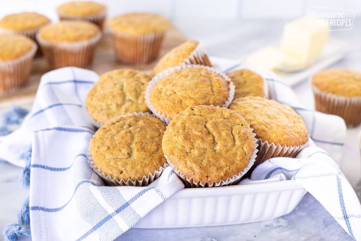 Container of Bran Muffins lined with a linen. Extra muffins in the background.