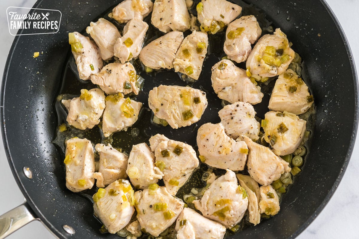 chicken cooking in a skillet with green onions