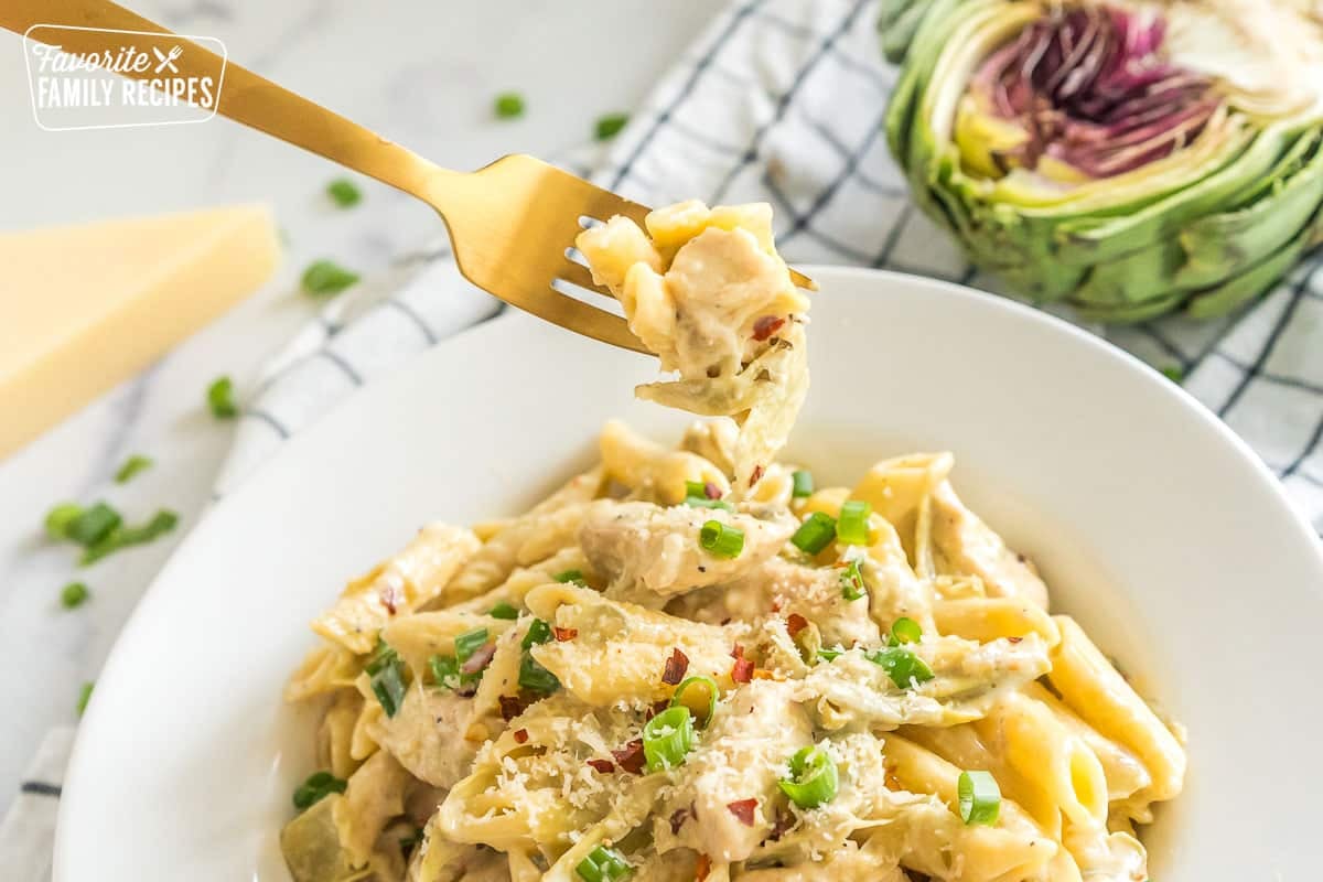 A forkful of penne with sauce being taken out of a bowl