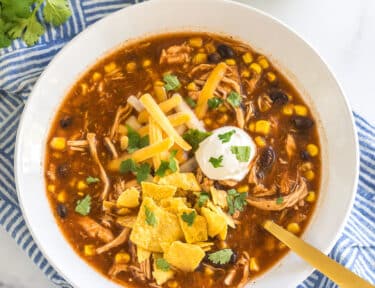 chicken taco soup in a bowl topped with sour cream, cheese, and tortilla chips