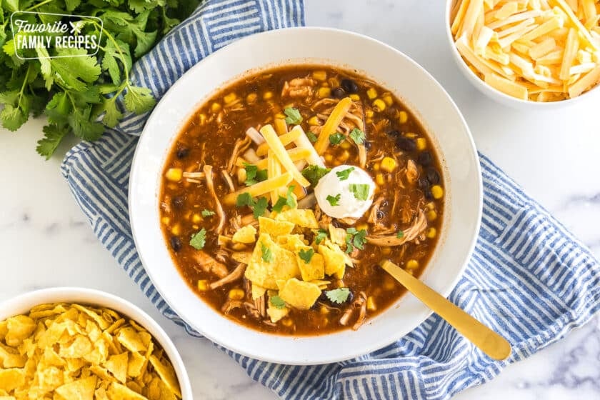 chicken taco soup in a bowl topped with sour cream, cheese, and tortilla chips