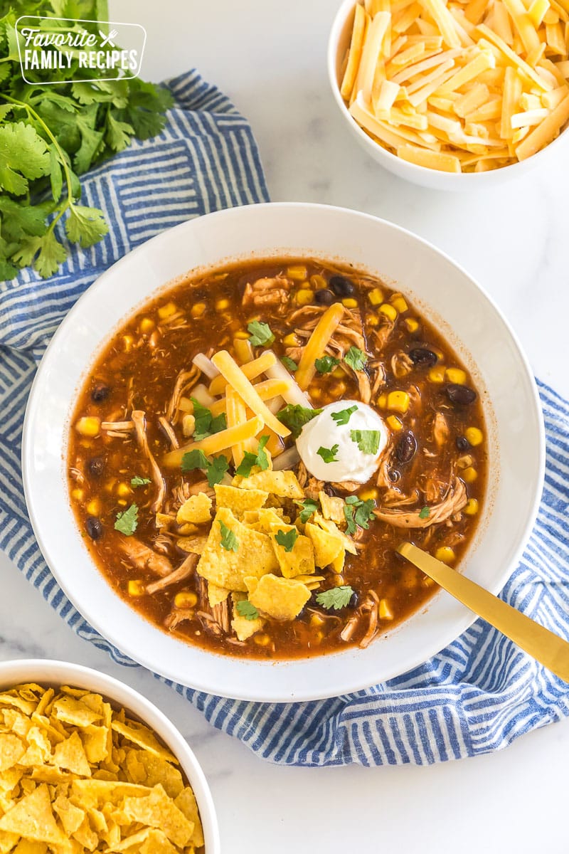 chicken taco soup in a bowl topped with sour cream, cheese, and tortilla chips