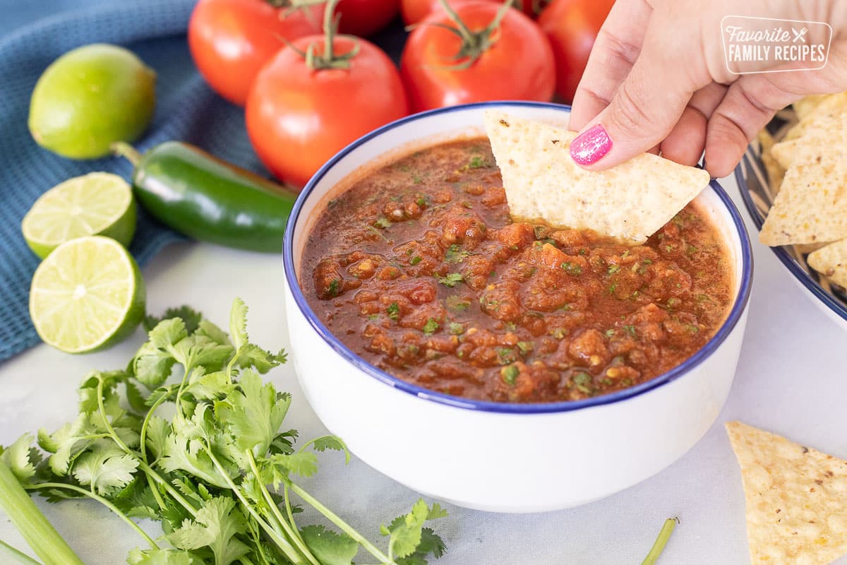 Dipping a chip into a bowl of Homemade Salsa with Fresh Tomatoes.