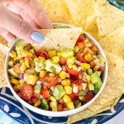 Hand Dipping a chip into a bowl for Fresh Corn Salsa.