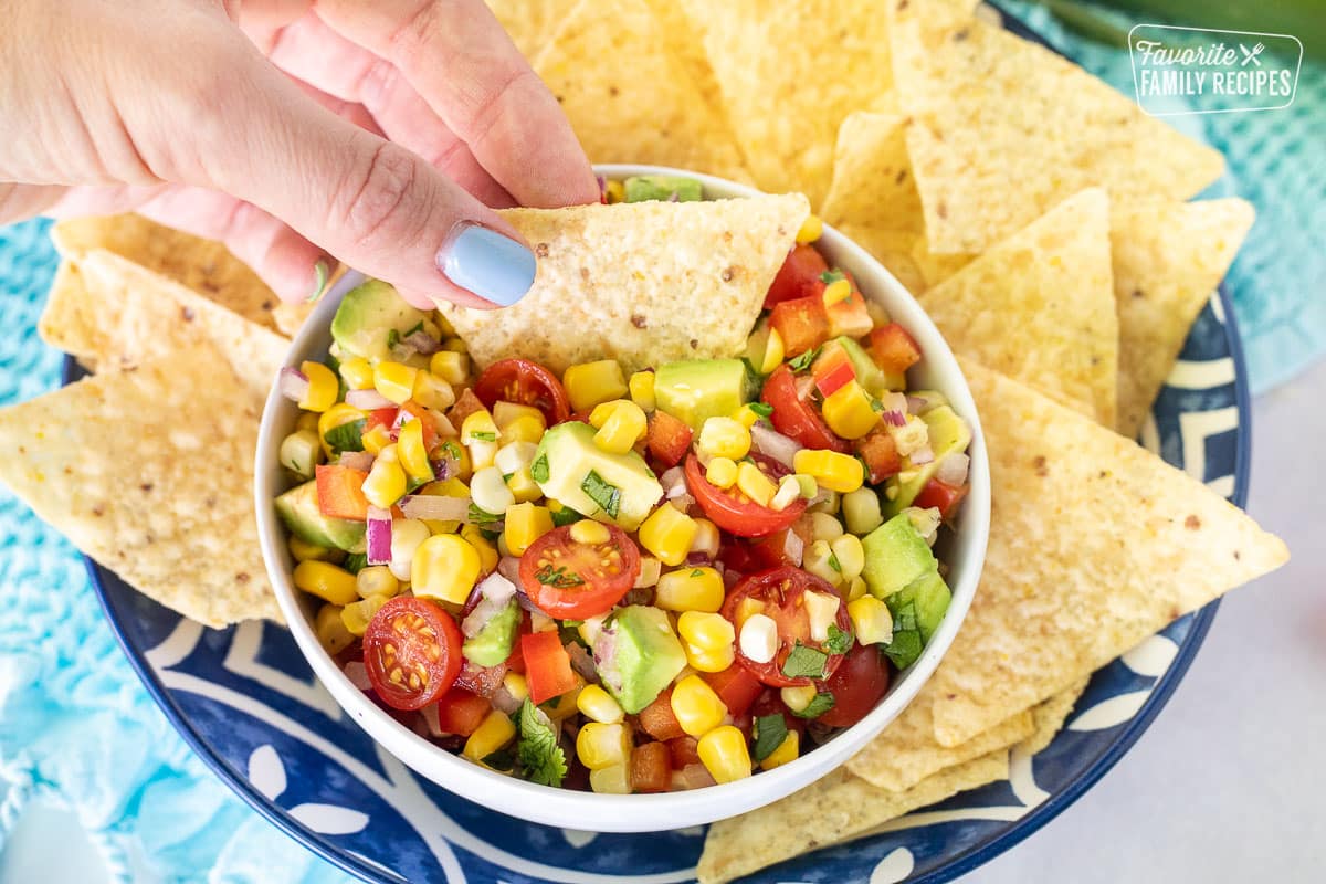 Hand Dipping a chip into a bowl for Fresh Corn Salsa.