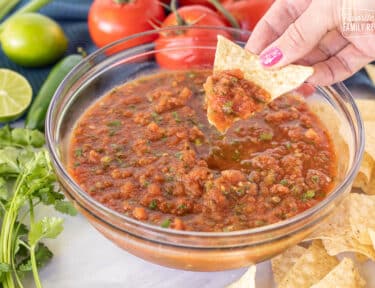 Hand holding a tortilla chip loaded with Fresh Tomato Homemade Salsa.