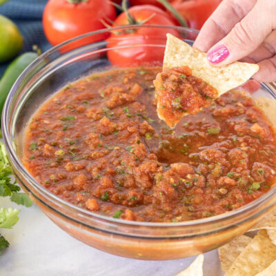 Hand holding a tortilla chip loaded with Fresh Tomato Homemade Salsa.