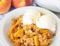 Dish of Crock Pot Peach Cobbler with two scoops of vanilla ice cream.