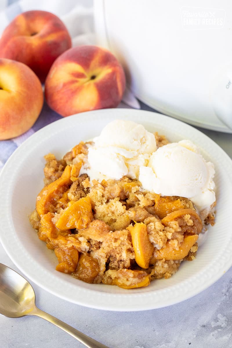 Dish of Crock Pot Peach Cobbler with two scoops of vanilla ice cream.