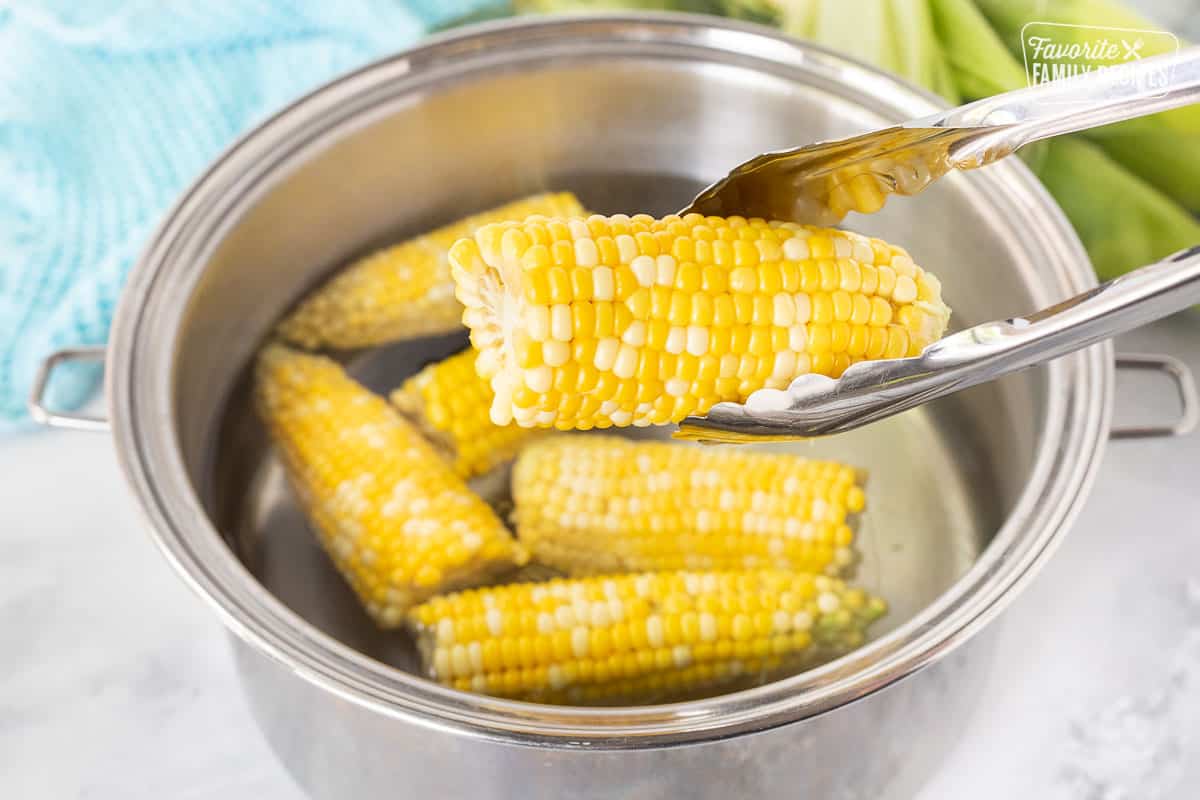 Tongs holding cooked corn on the cob over a pot of hot water for Fresh Salsa.