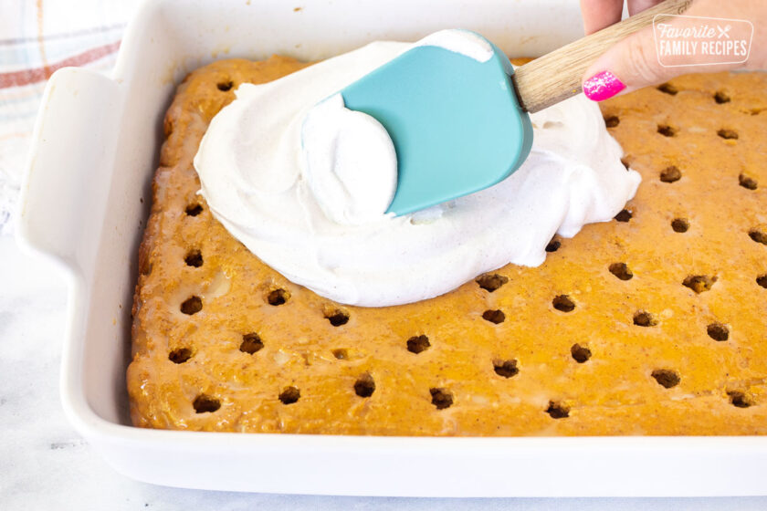 Spreading cinnamon Cool Whip on top of Pumpkin Poke Cake with a spatula.