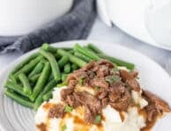 Plate with Crockpot Steak and Gravy over mashed potatoes and green beans on the side.