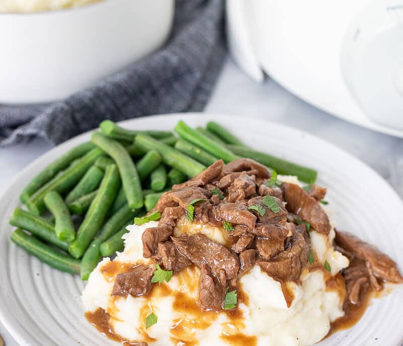 Plate with Crockpot Steak and Gravy over mashed potatoes and green beans on the side.