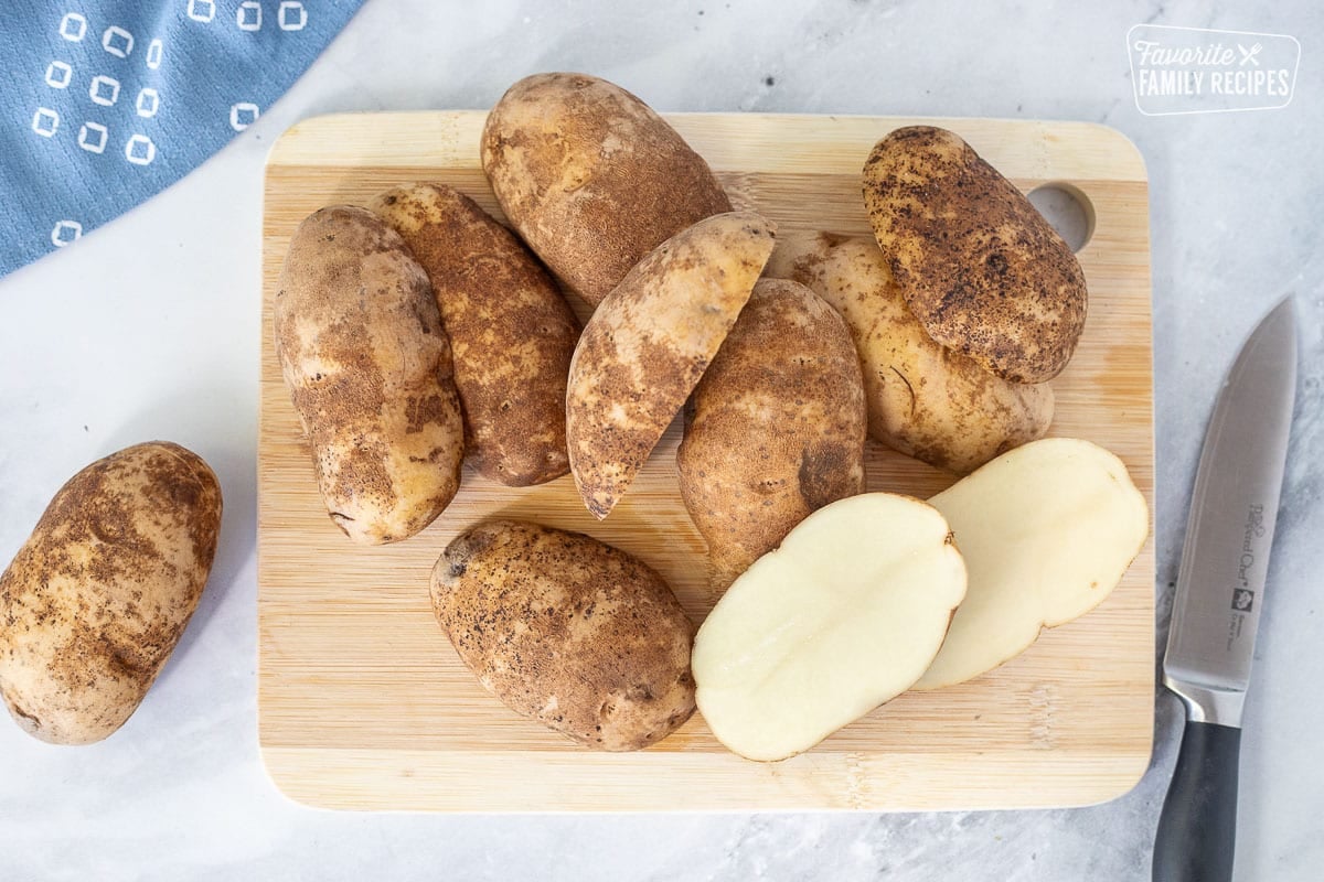 Cutting board with russet potatoes cut in half with a knife.