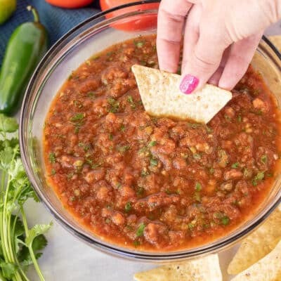 Hand dipping a tortilla chip into a bowl of Homemade Salsa with Fresh Tomatoes.