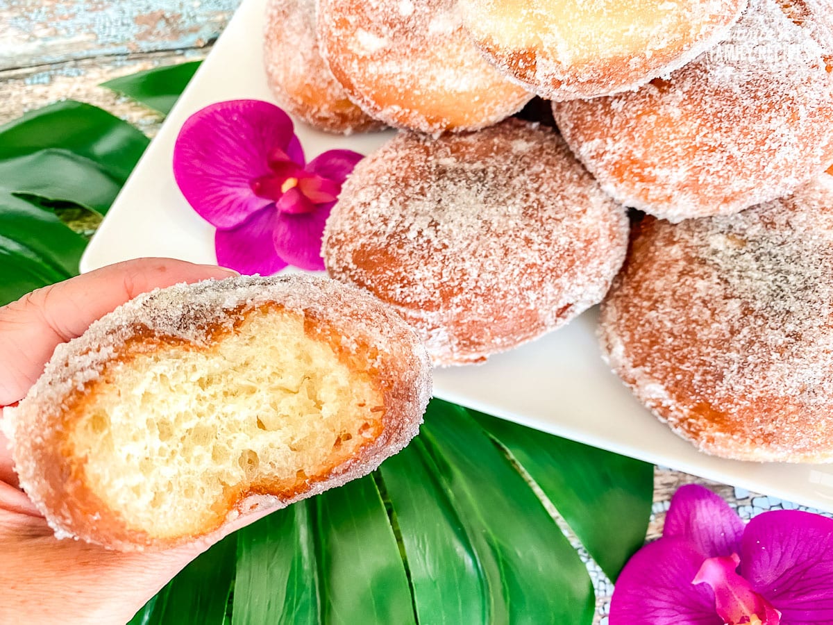 A hand holding a malasada with a bite taken out of it to show fluffy texture