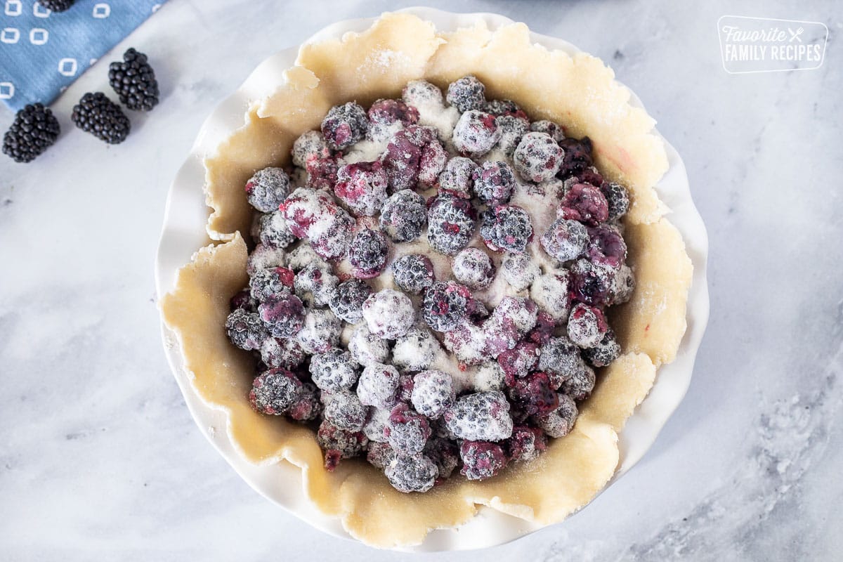 Pie dish with crust and blackberry pie filling.