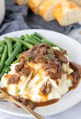 Plate with Crockpot Steak and Gravy, mashed potatoes and fork. Green beans on the side.