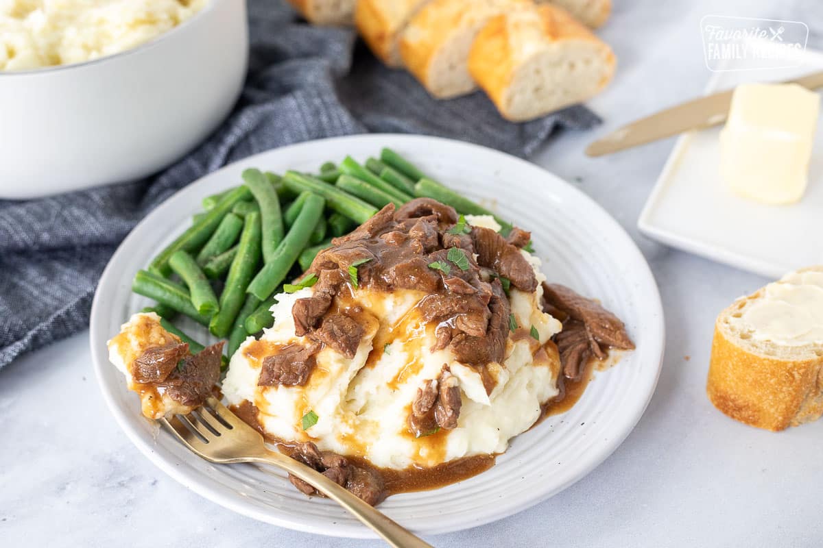 Plate with Crockpot Steak and Gravy, mashed potatoes and fork. Green beans on the side.