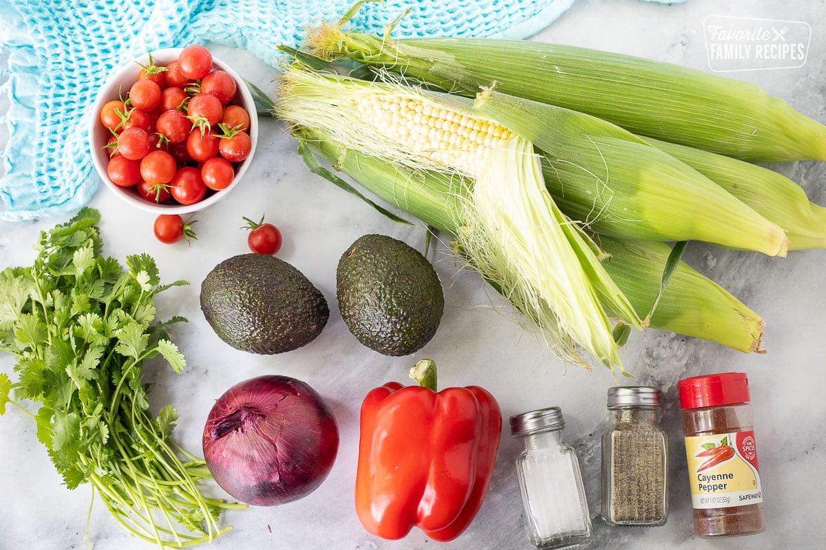 Ingredients to make Fresh Corn Salsa including cherry tomatoes, corn, avocado, cilantro, red onion, red bell pepper, salt, pepper and cayenne pepper.