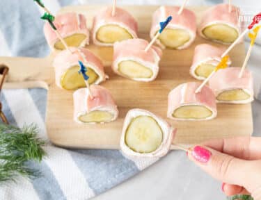 Hand holding a Pickle wrapped in cream cheese and Ham with a toothpick.