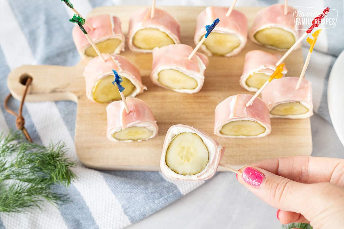 Hand holding a Pickle wrapped in cream cheese and Ham with a toothpick.