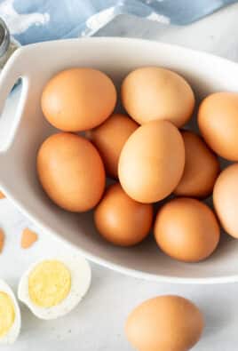 Bowl of Instant Pot Boiled Eggs next to salt and pepper and boiled egg cut in two.