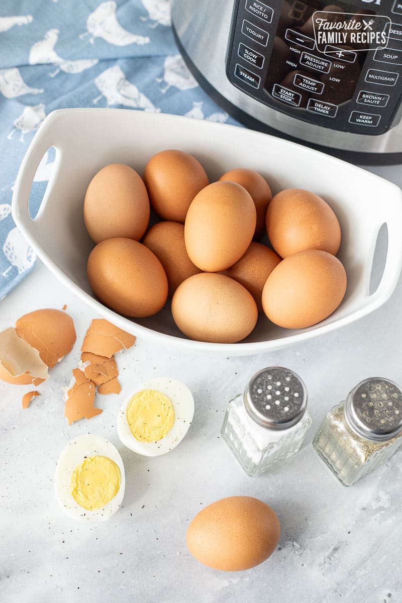 Bowl of Instant Pot Boiled Eggs next to a sliced open boiled egg with salt and pepper.