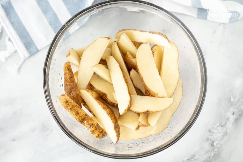 Mixing bowl of Potato Wedges with oil.