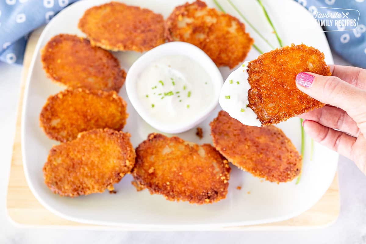 Hand holding a Parmesan Crusted Potato dipped in sour cream and chives.