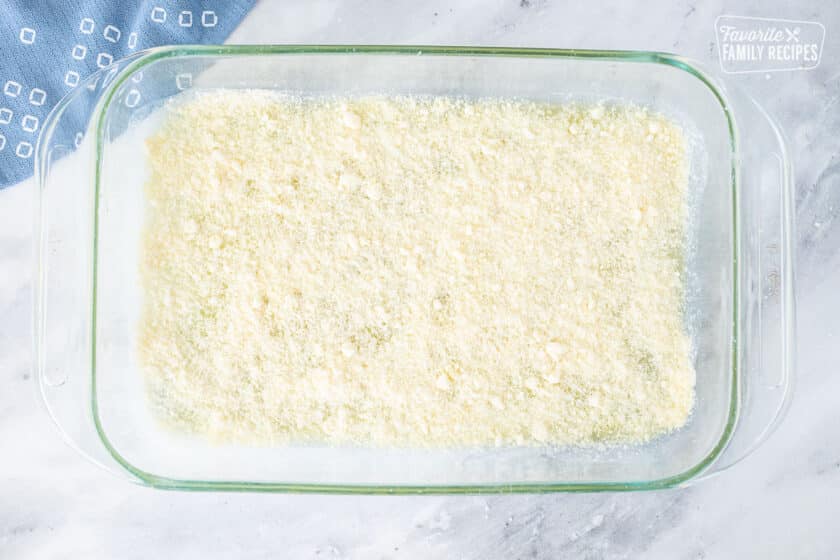 Baking dish with parmesan cheese on top of melted butter for Parmesan Crusted Potatoes.