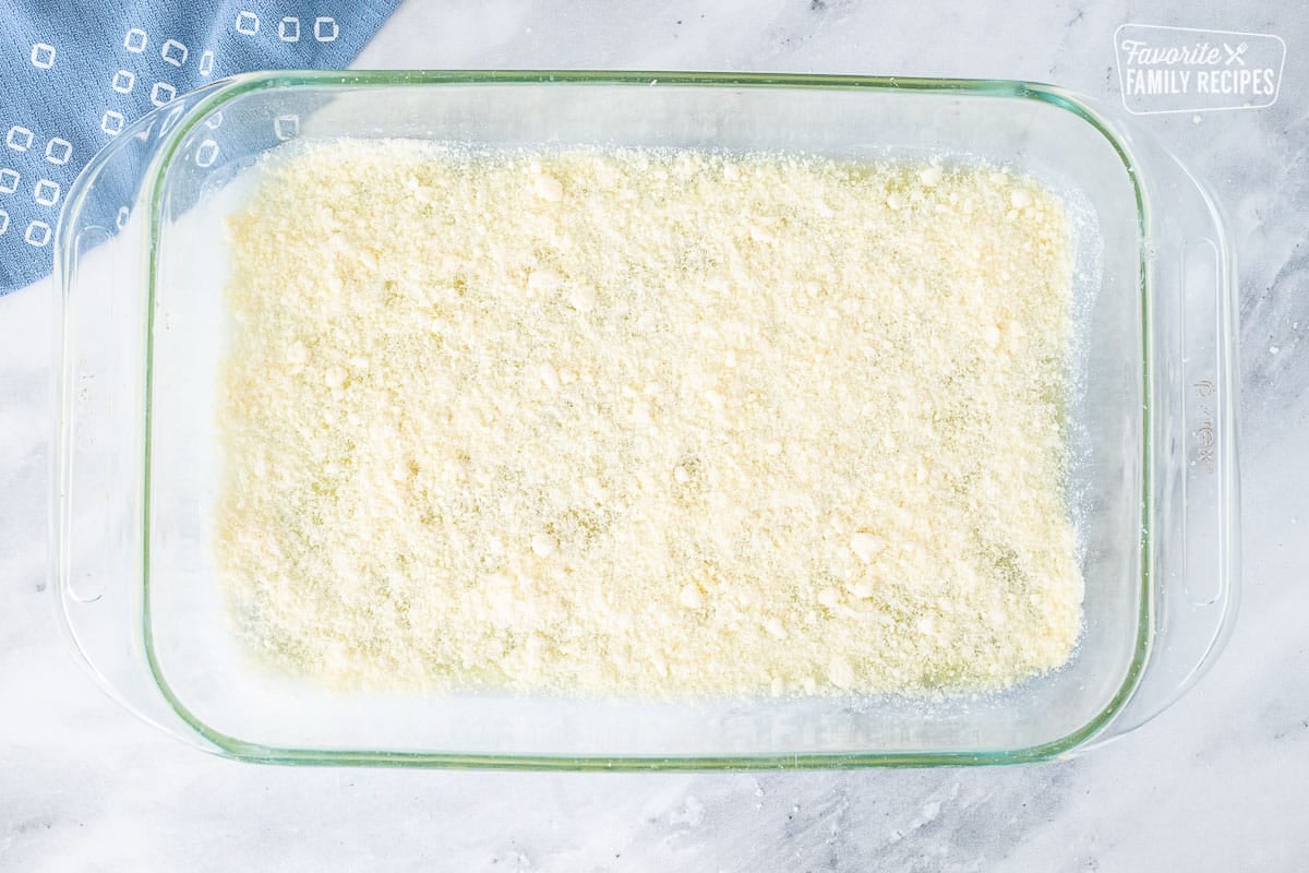 Baking dish with parmesan cheese on top of melted butter for Parmesan Crusted Potatoes.