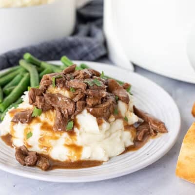 Crockpot Steak and Gravy over mashed potatoes and garnished with parsley. Baguette bread on the side.