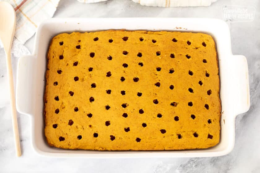 Holes poked in the Pumpkin Cake in a baking dish. Wooden spoon on the side.