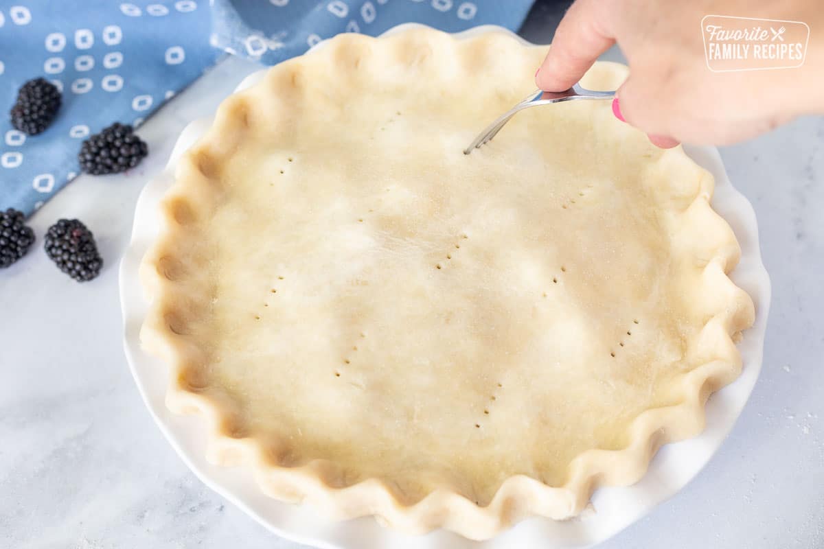 Poking holes with a fork on the top of the pie crust.