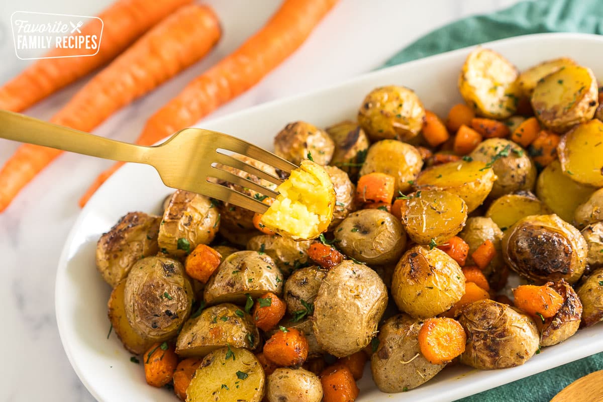 Roasted Potatoes and Carrots on a platter with a fork taking one of the potatoes with a bite out of it.
