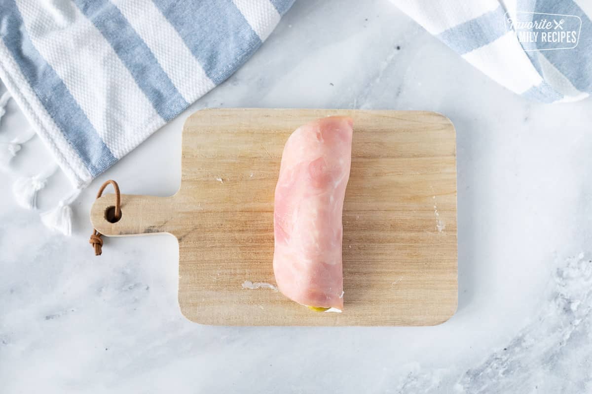 Cutting board with ham rolled up around a pickle.