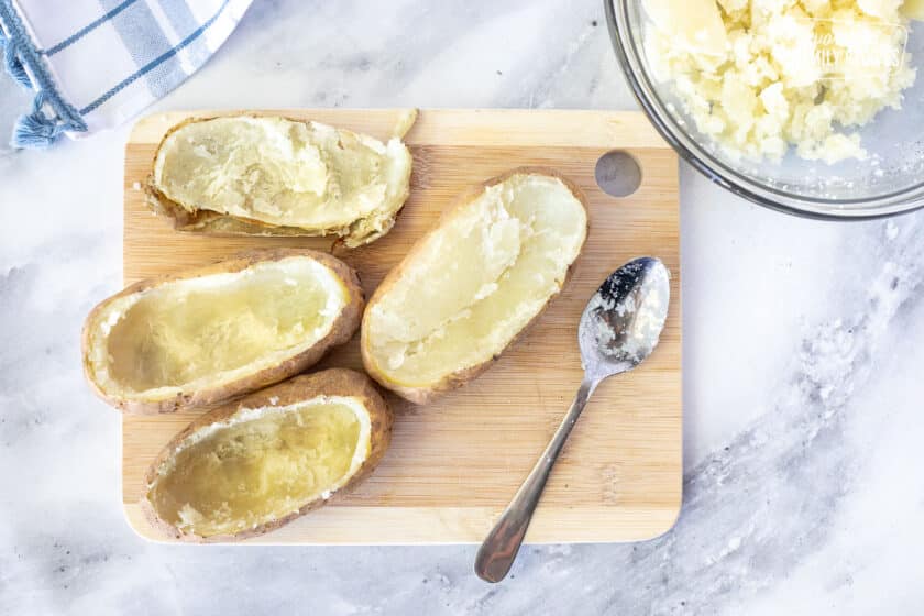 Cutting board with a spoon scooping out baked potatoes for Twice Baked Potatoes.