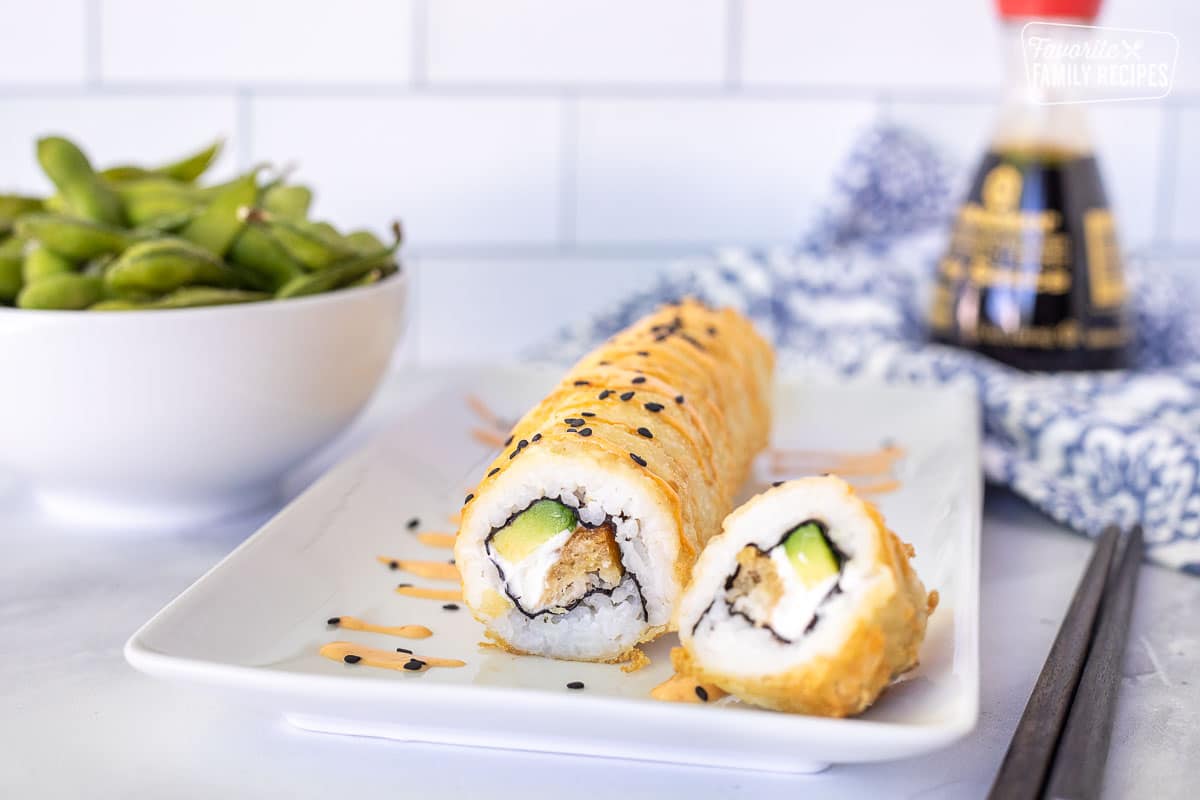 Shrimp Tempura Roll on a plate topped with spicy mayo and black sesame seeds.