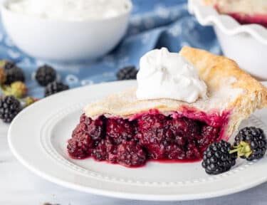 Slice of Blackberry Pie topped with whipped cream.