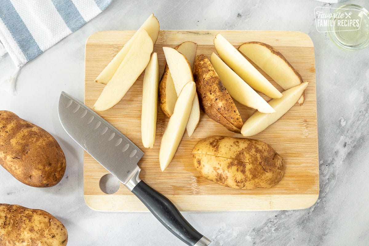 Slicing potatoes on cutting board with a knife for Loaded Potato Wedges.