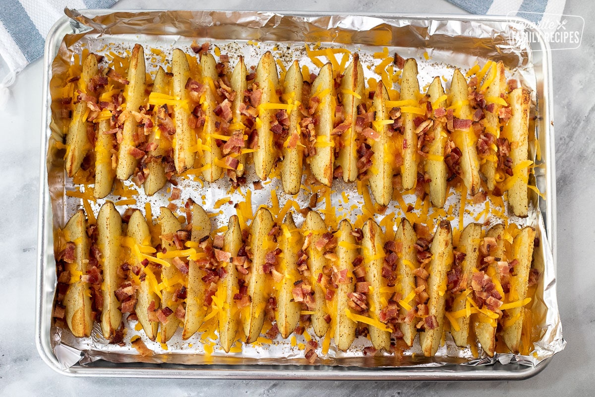 Baked Potato Wedges on a cookie sheet with unmelted cheese and bacon bits on top.