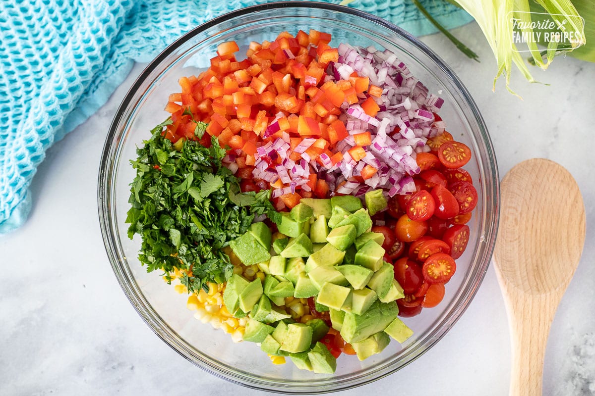 Bowl with corn, red bell pepper, red onion, cherry tomatoes, cilantro and avocado for Fresh Corn Salsa.