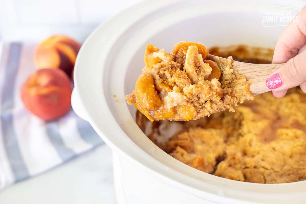 Wooden spoon dishing up Peach Cobbler from the Crock Pot.
