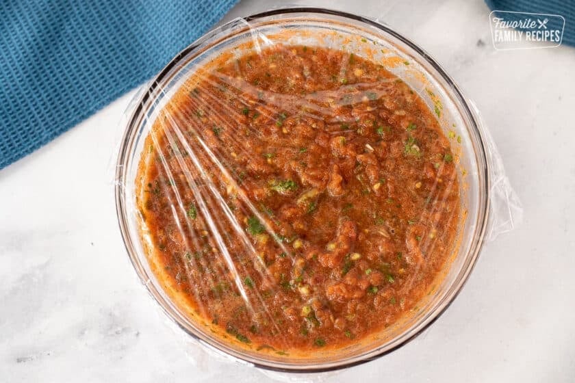 Plastic wrap over the bowl of Homemade Salsa with Fresh Tomatoes.