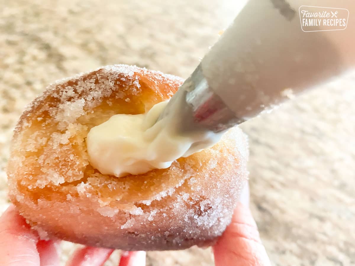 A malasada being filled with coconut haupia filling using a piping bag