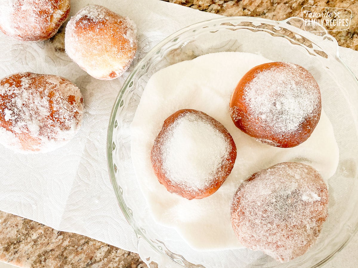 Malasadas placed in a shallow dish of sugar to make the sugary coating