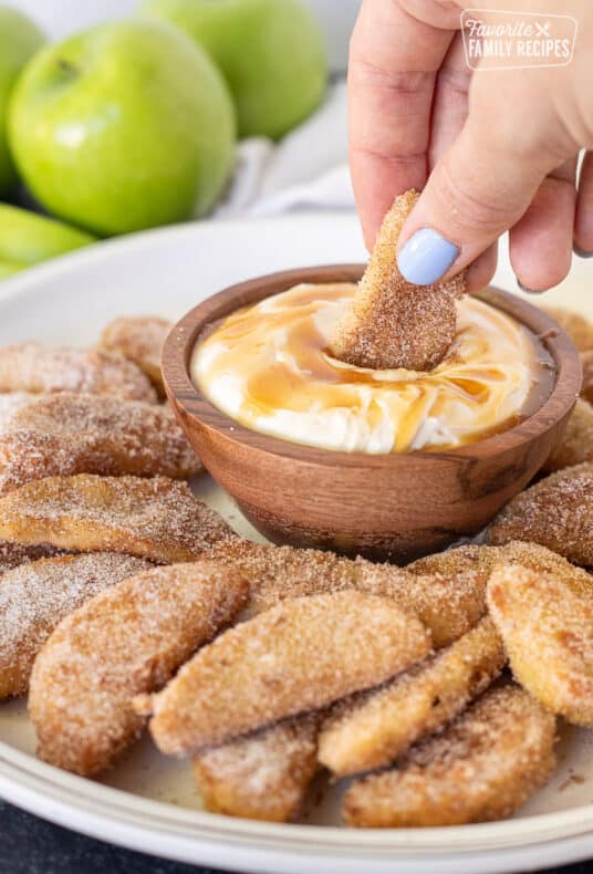 Hand holding a Apple Fry and dipping it into caramel dip.